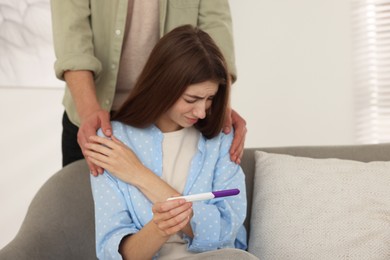 Photo of Upset woman with negative pregnancy test indoors. Man supporting his wife at home