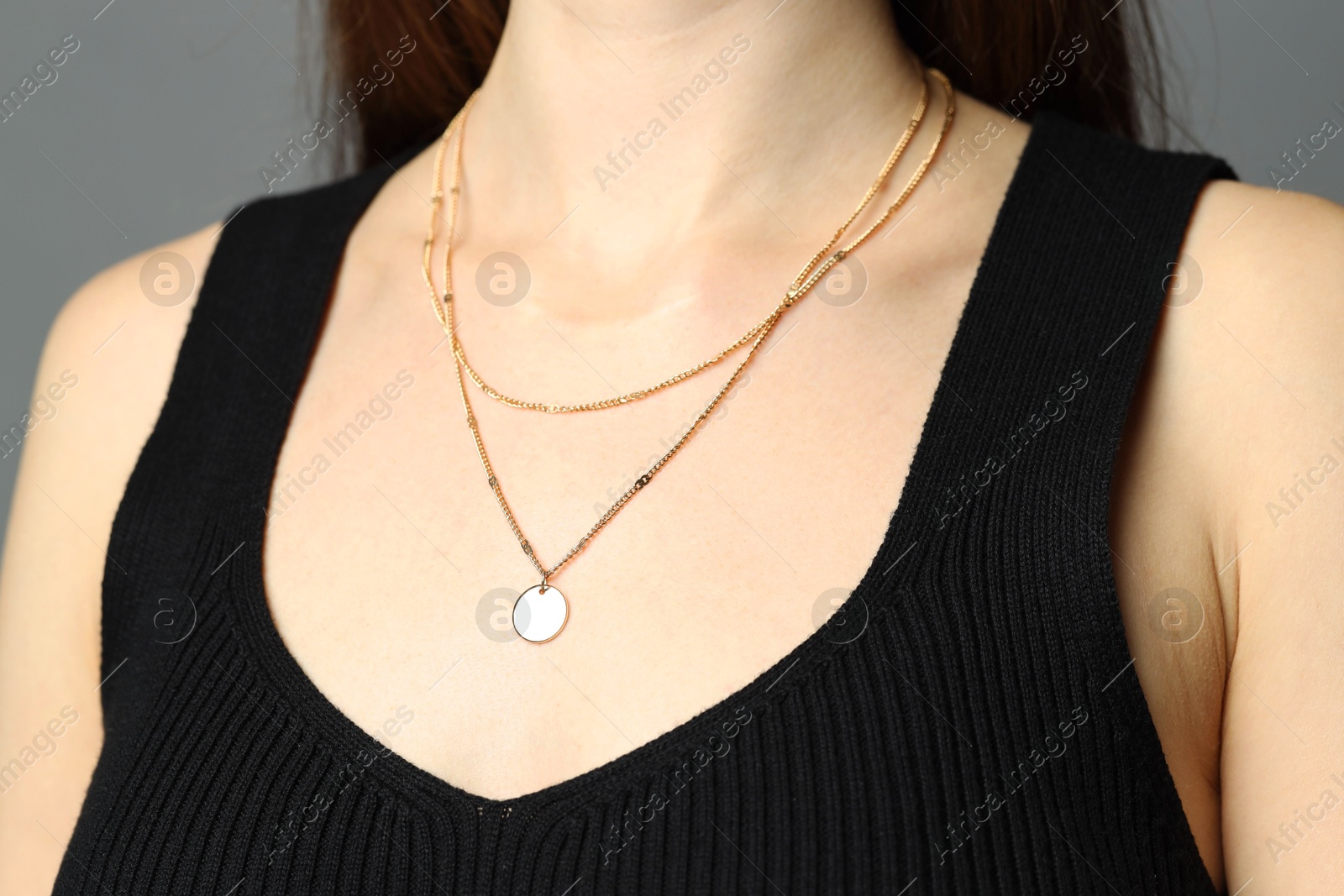 Photo of Woman wearing layered golden necklace on grey background, closeup