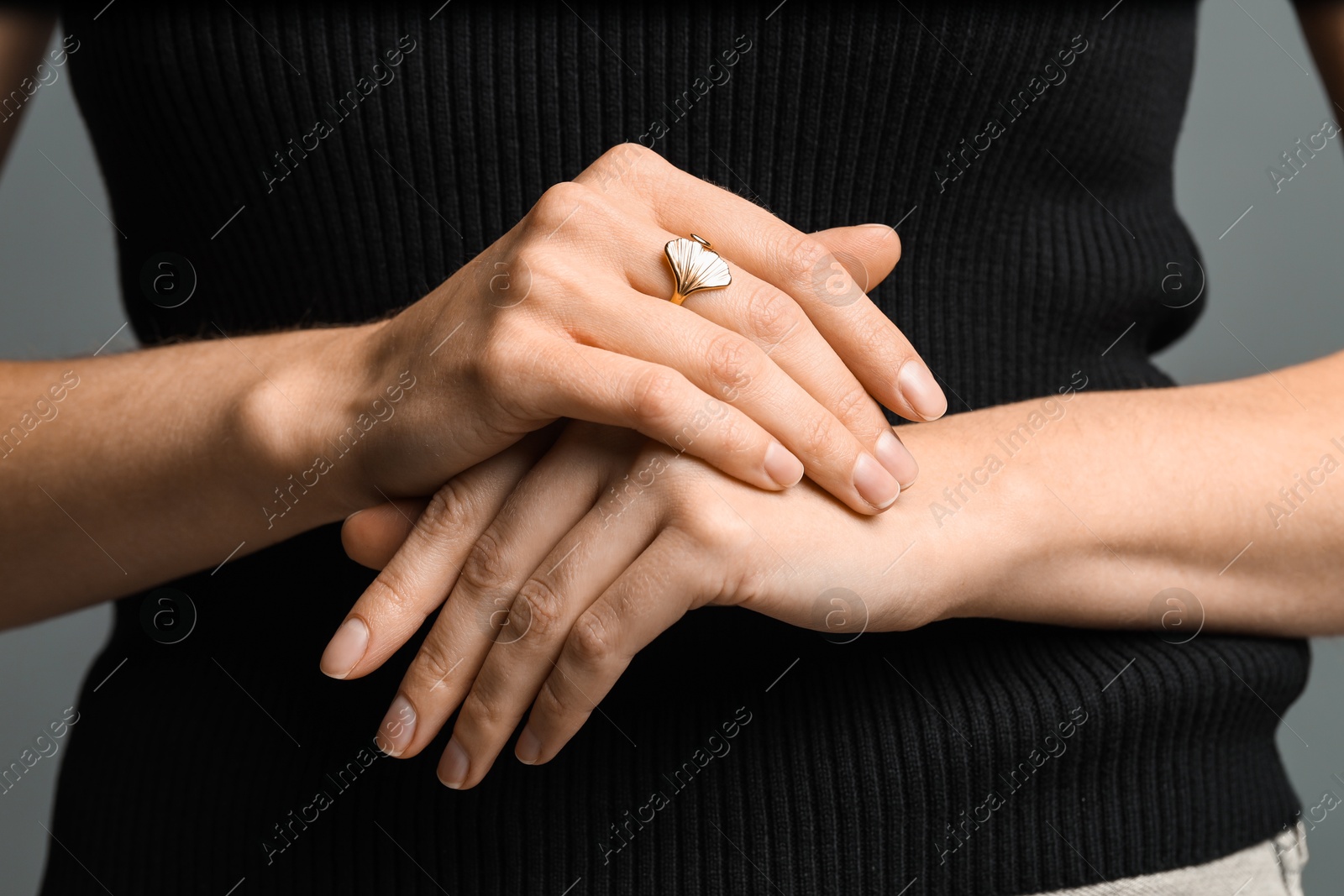 Photo of Woman wearing beautiful golden ring on grey background, closeup