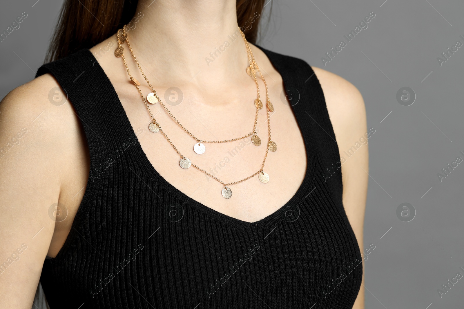 Photo of Woman wearing layered golden necklace on grey background, closeup