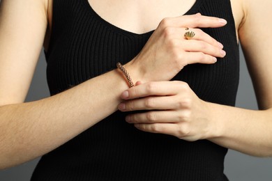 Photo of Woman wearing elegant golden bracelet and ring on grey background, closeup