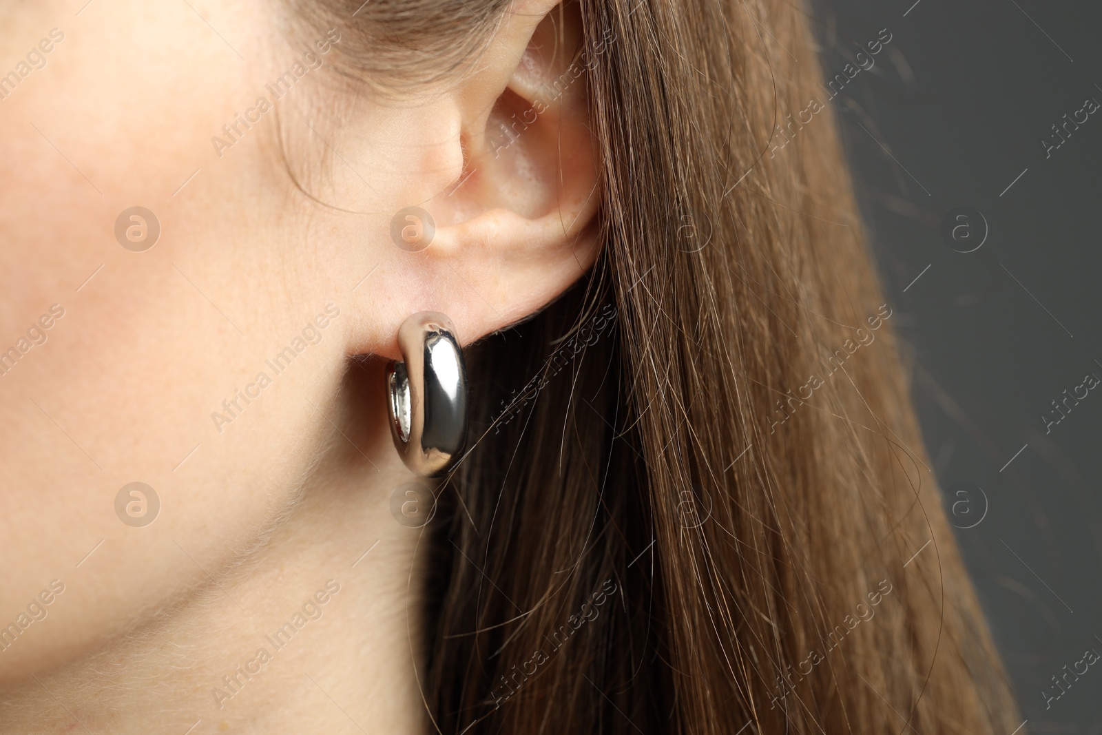 Photo of Woman wearing beautiful silver earring on grey background, closeup