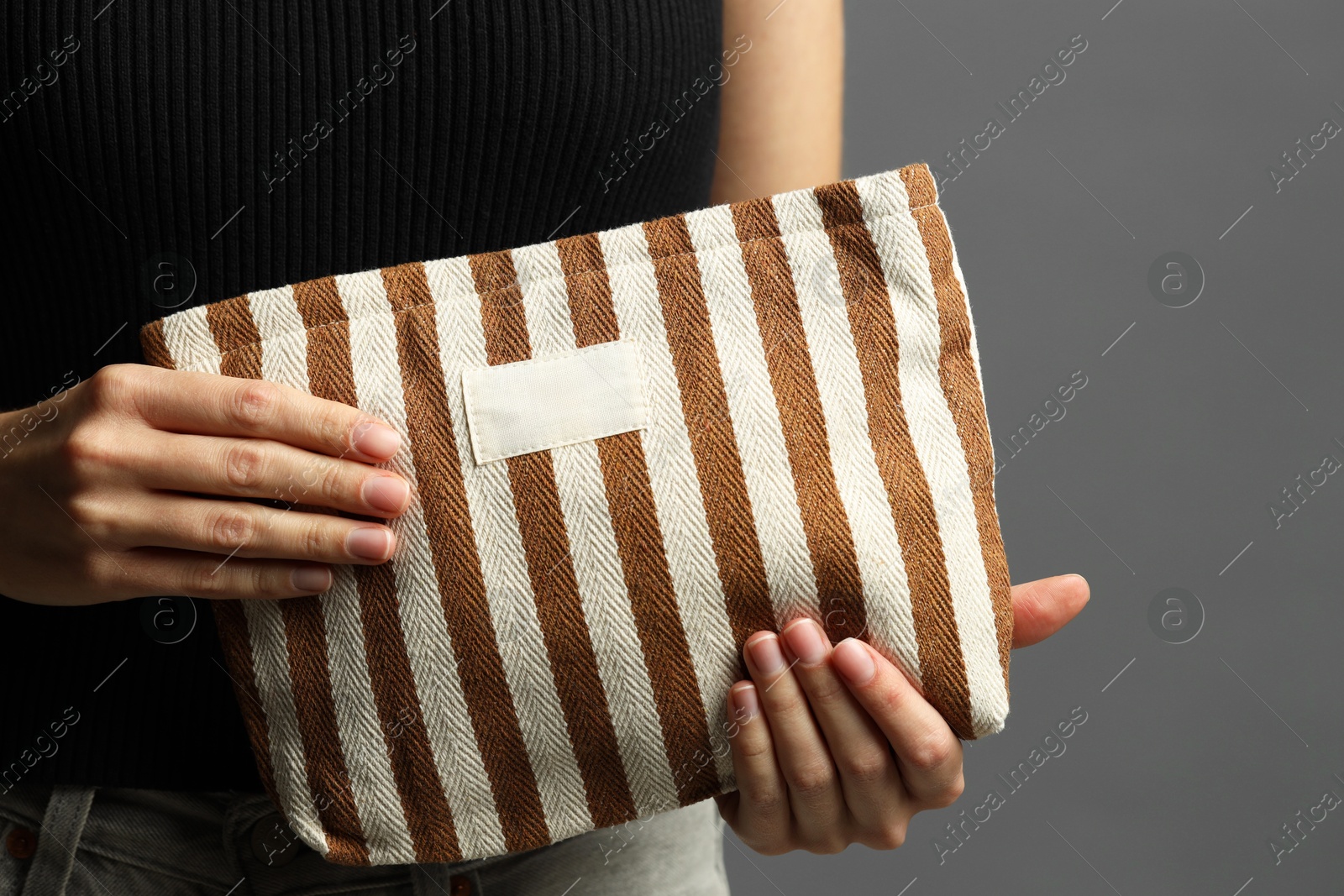 Photo of Woman with striped cosmetic bag on grey background, closeup