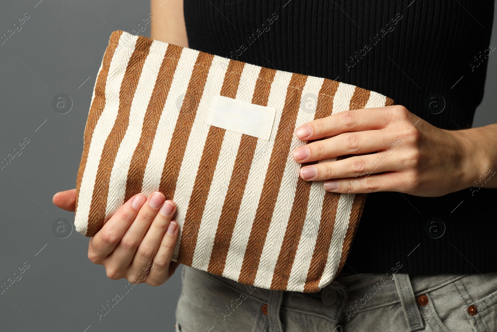 Photo of Woman with striped cosmetic bag on grey background, closeup