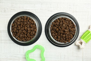 Photo of Dry pet food in feeding bowls and toys on floor, flat lay