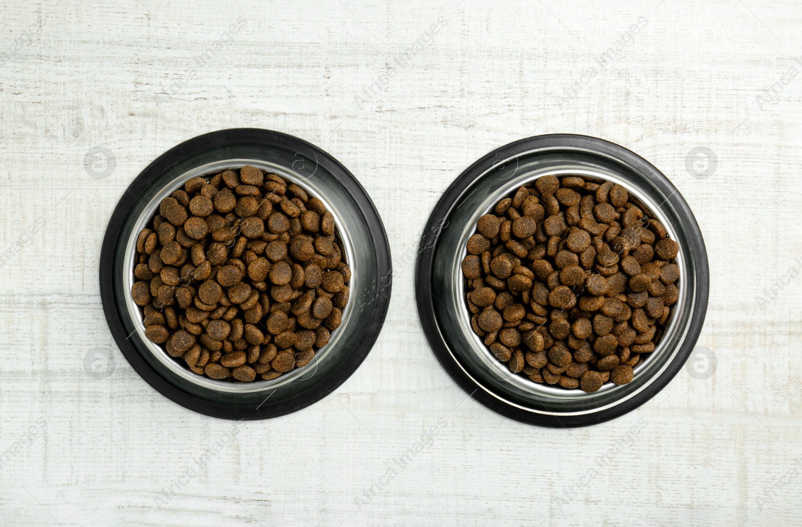 Photo of Dry pet food in feeding bowls on floor, top view