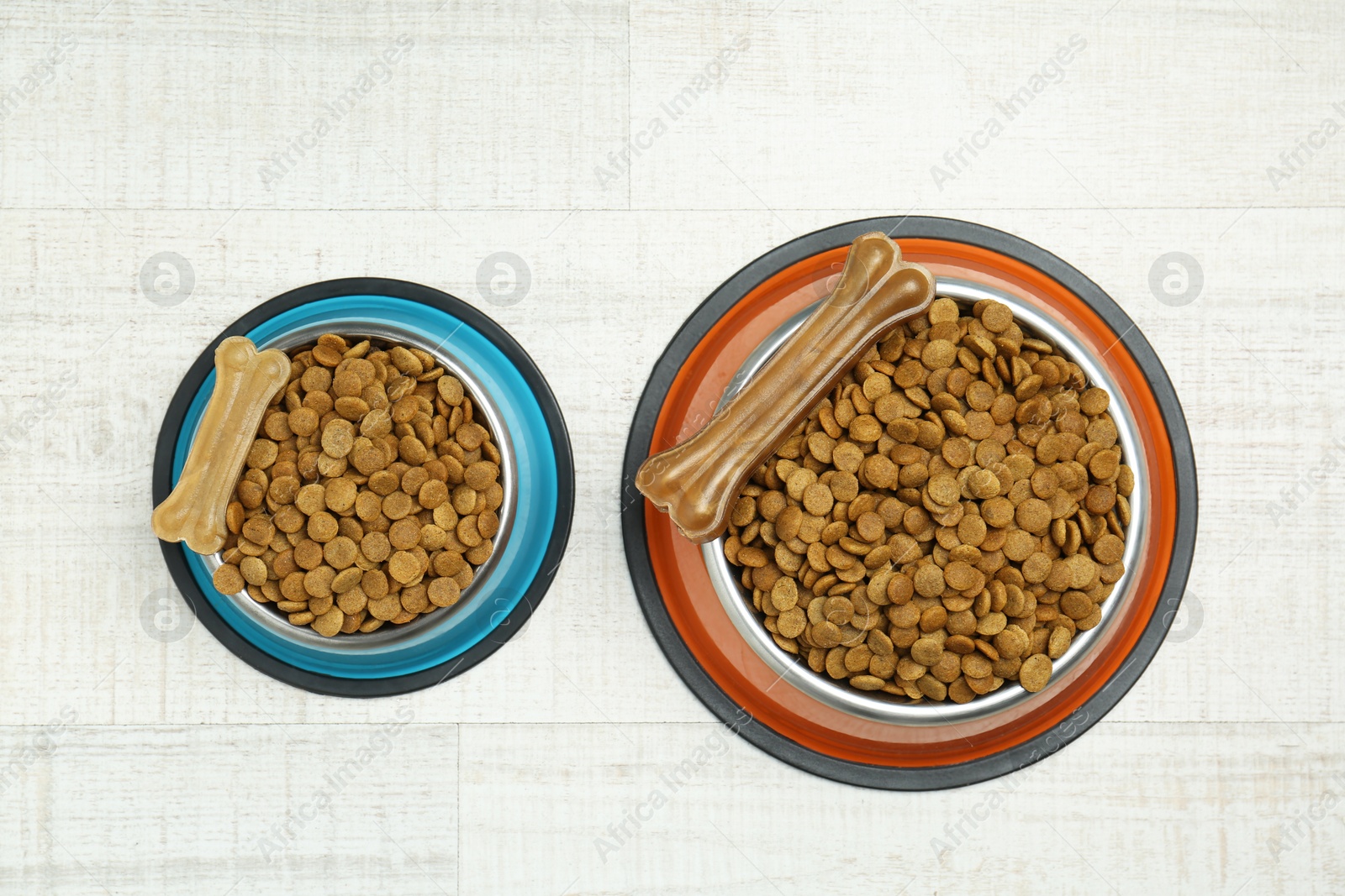 Photo of Dry pet food in feeding bowls and chew bones on floor, top view