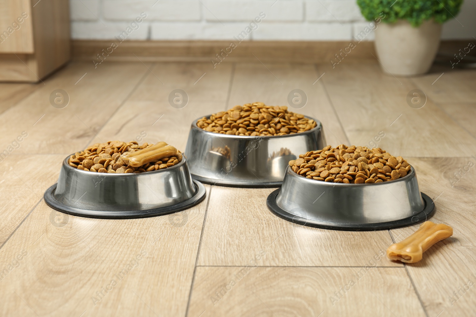 Photo of Dry pet food in feeding bowls and chew bones on floor indoors