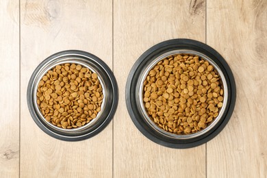 Photo of Dry pet food in feeding bowls on wooden floor, top view