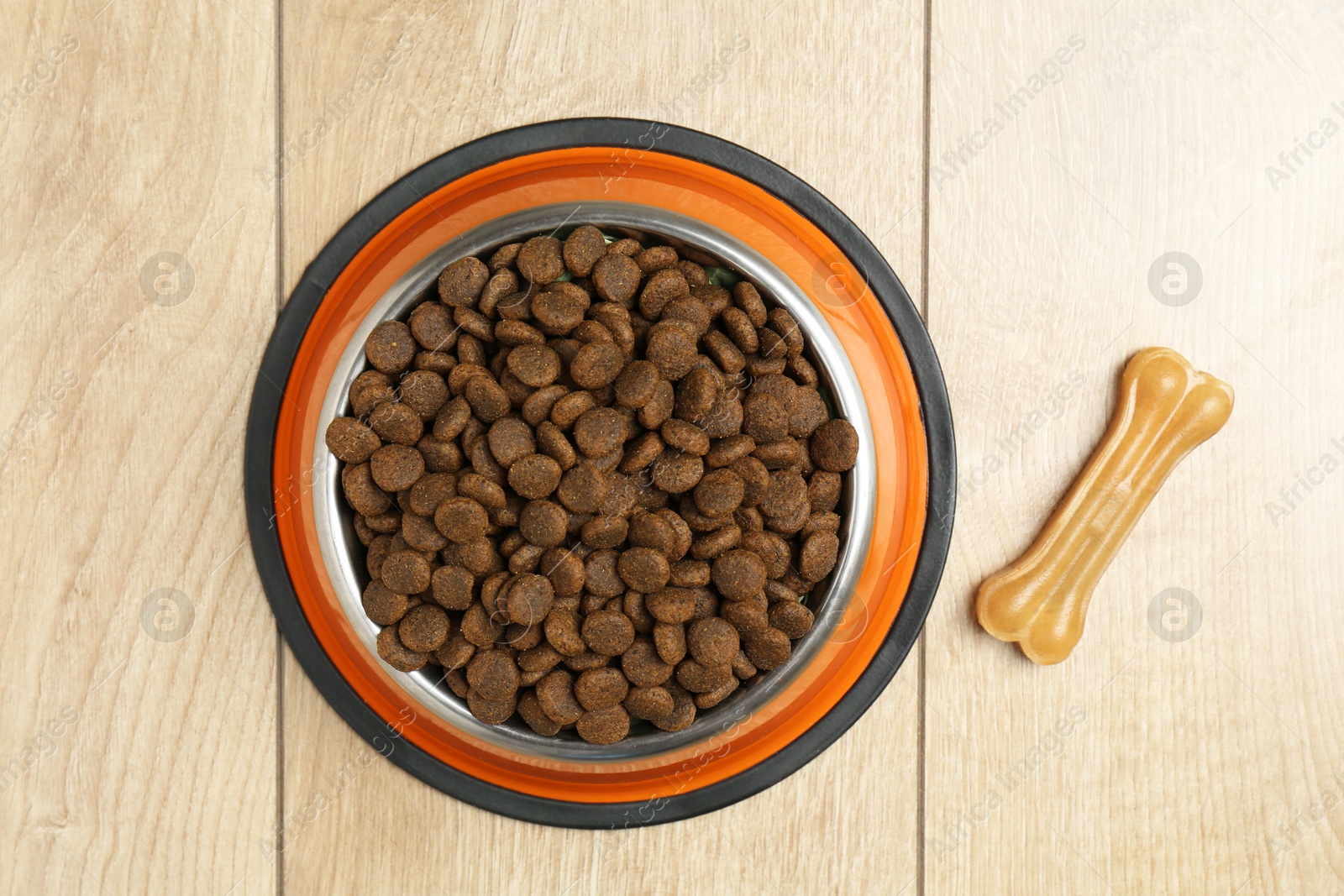 Photo of Dry pet food in feeding bowl and chew bone on wooden floor, top view