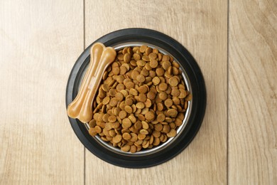 Photo of Dry pet food in feeding bowl and chew bone on wooden floor, top view