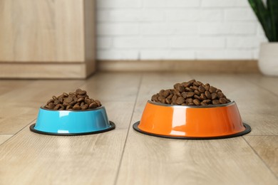 Photo of Dry pet food in feeding bowls on floor indoors