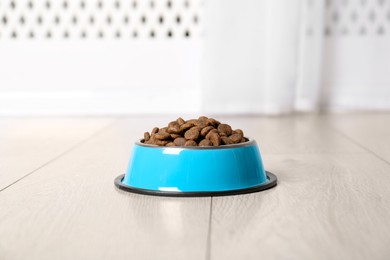 Photo of Dry pet food in feeding bowl on floor indoors