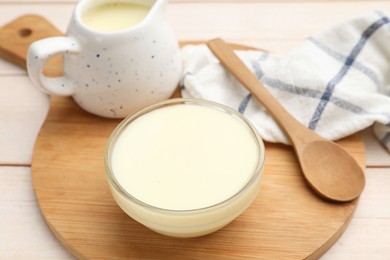 Photo of Condensed milk and spoon on light wooden table, closeup