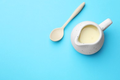 Photo of Tasty condensed milk in jug and spoon on light blue background, top view. Space for text