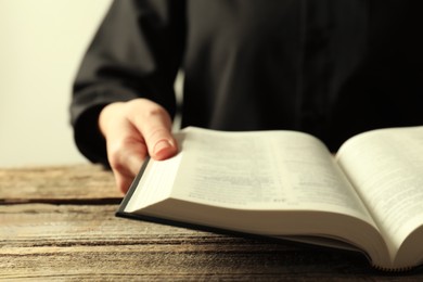 Woman with Holy Bible in English language at wooden table, closeup