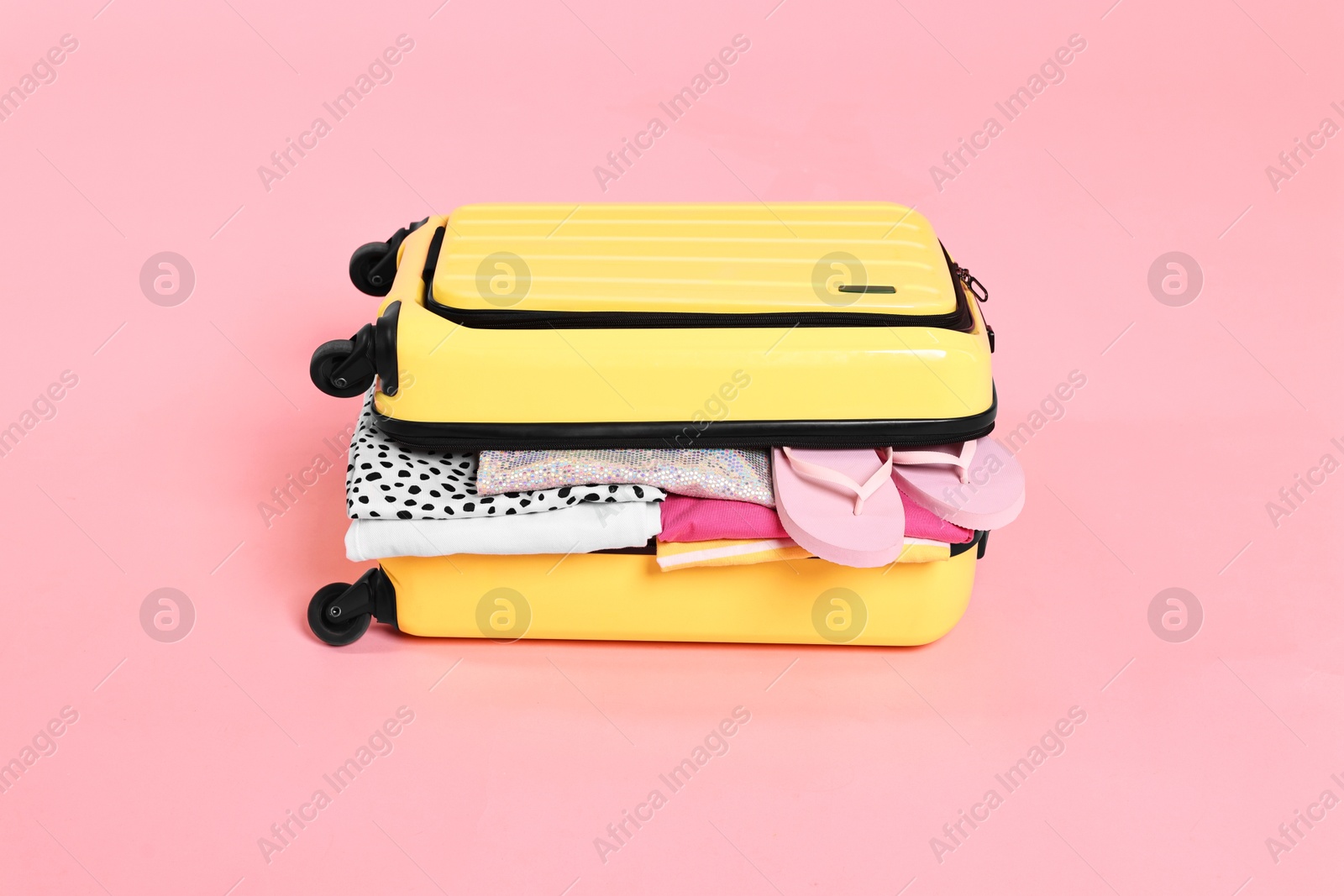 Photo of Packed suitcase full of clothes on pink background