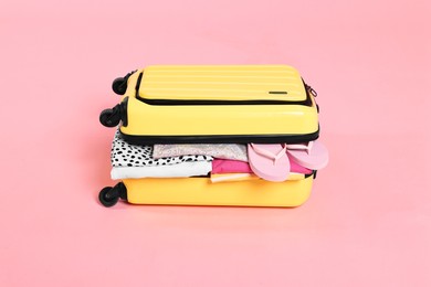 Photo of Packed suitcase full of clothes on pink background