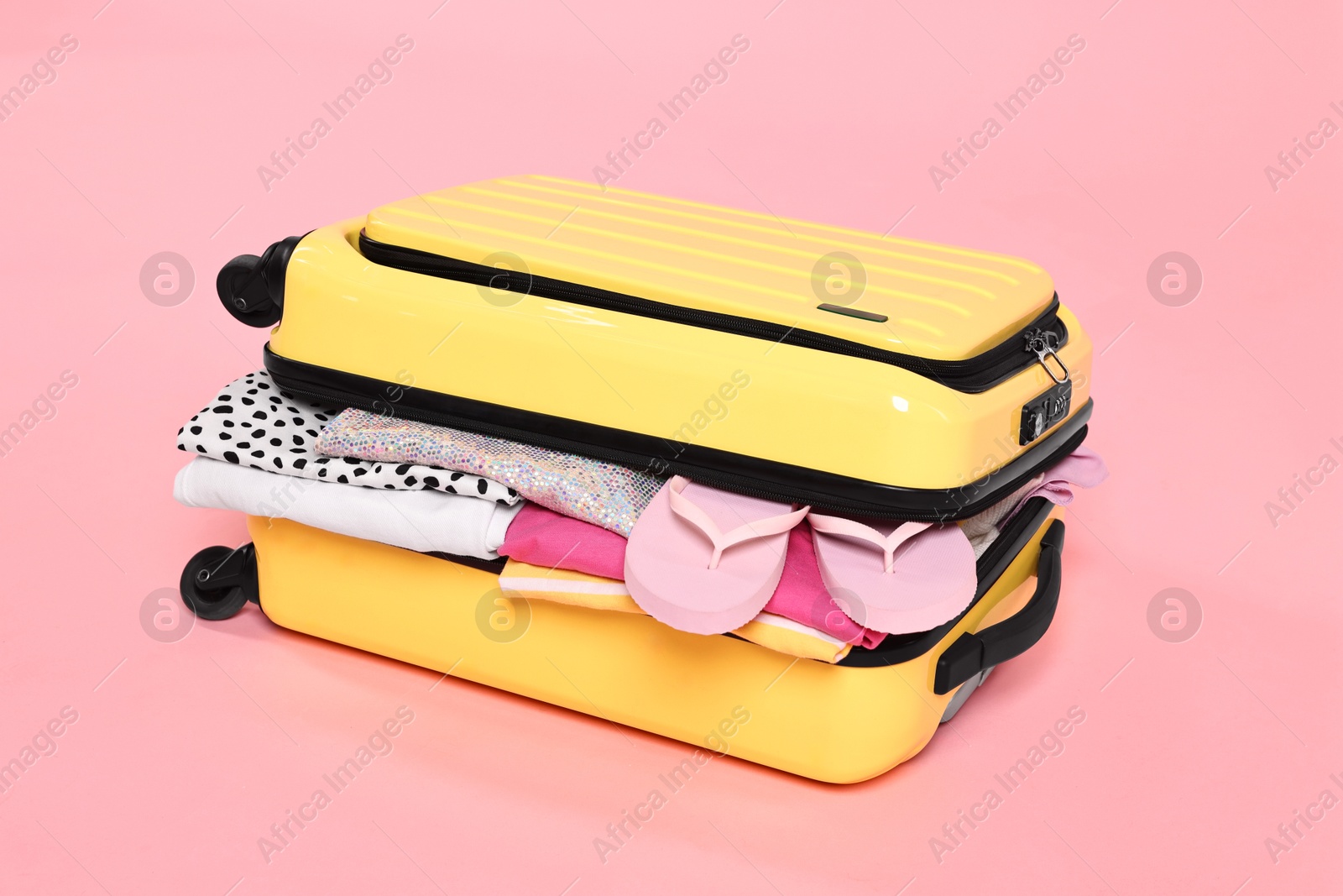 Photo of Packed suitcase full of clothes on pink background