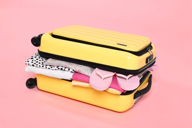 Photo of Packed suitcase full of clothes on pink background