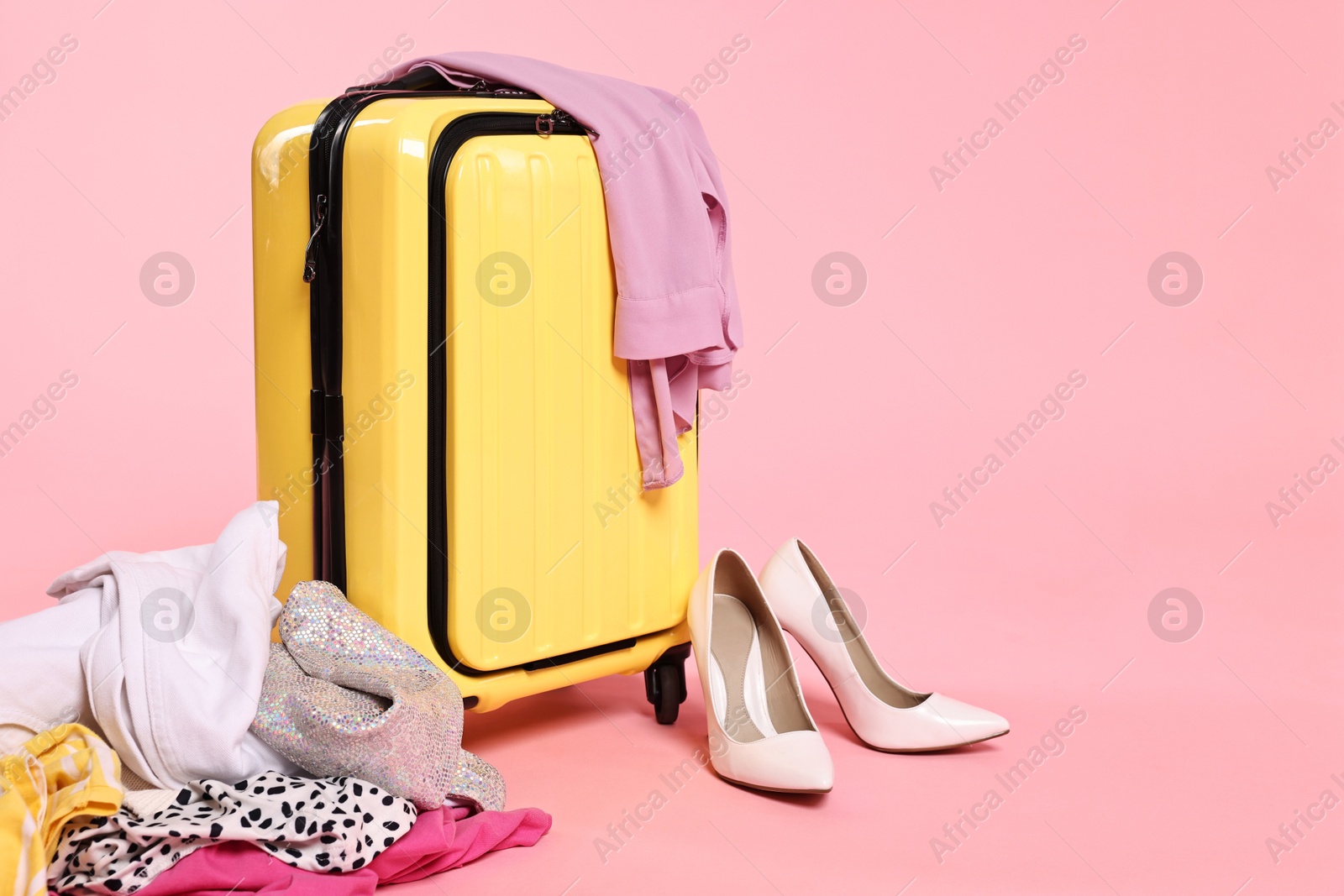 Photo of Suitcase, messy clothes and shoes on pink background