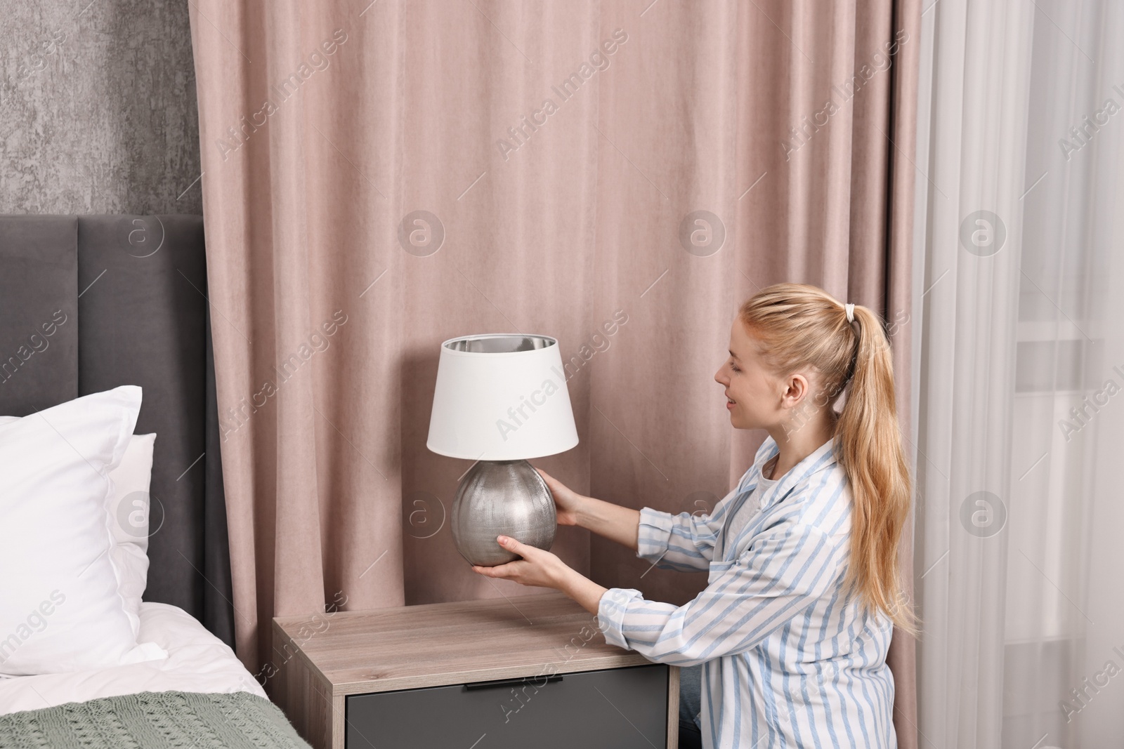 Photo of Female decorator arranging lamp onto nightstand in bedroom