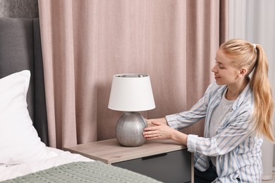 Photo of Smiling decorator arranging lamp onto nightstand in bedroom