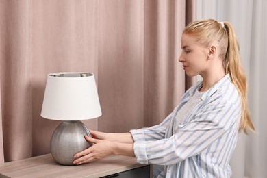 Photo of Female decorator arranging lamp onto nightstand indoors