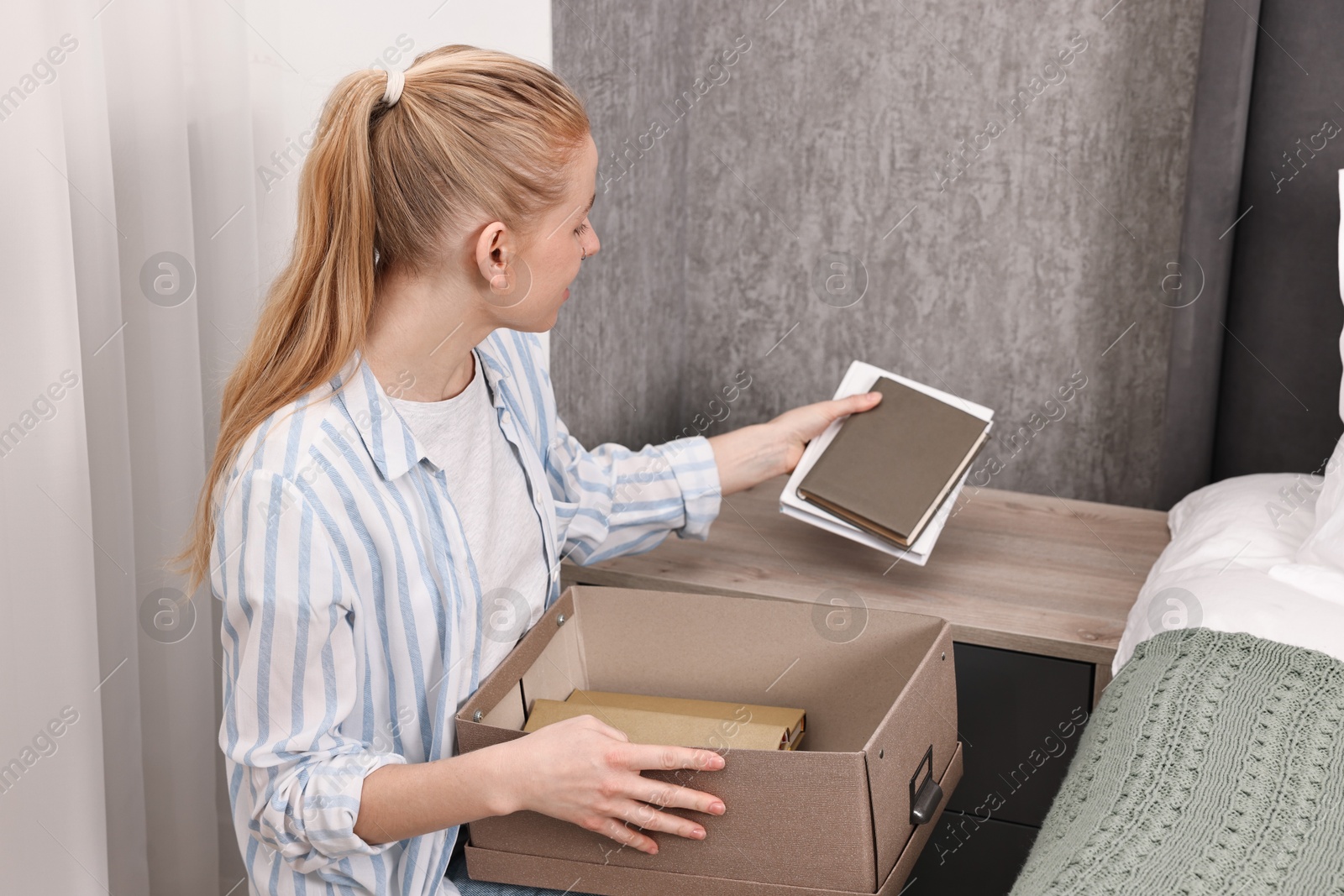 Photo of Female decorator arranging books onto nightstand indoors