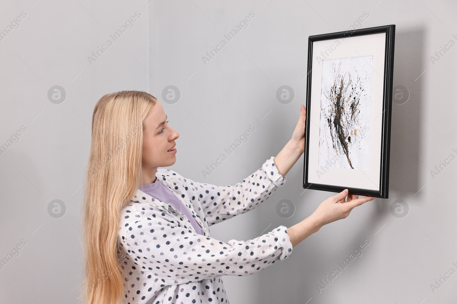 Photo of Smiling decorator hanging abstract picture on wall indoors