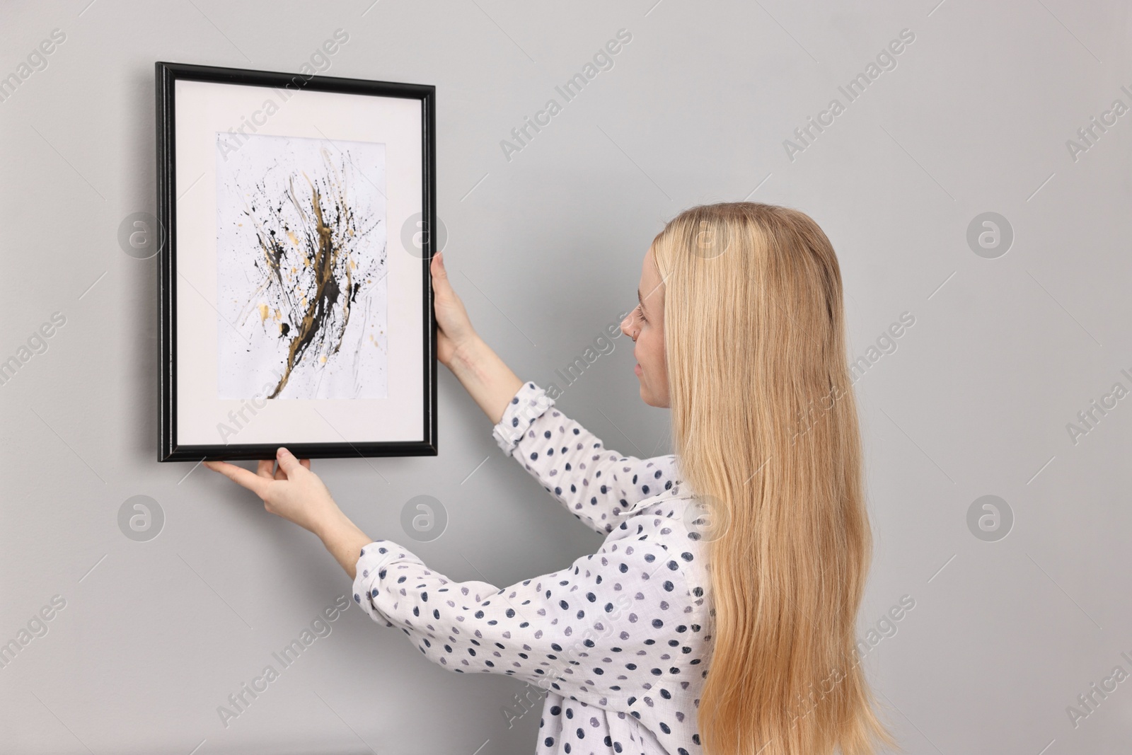 Photo of Female decorator hanging abstract picture on wall indoors