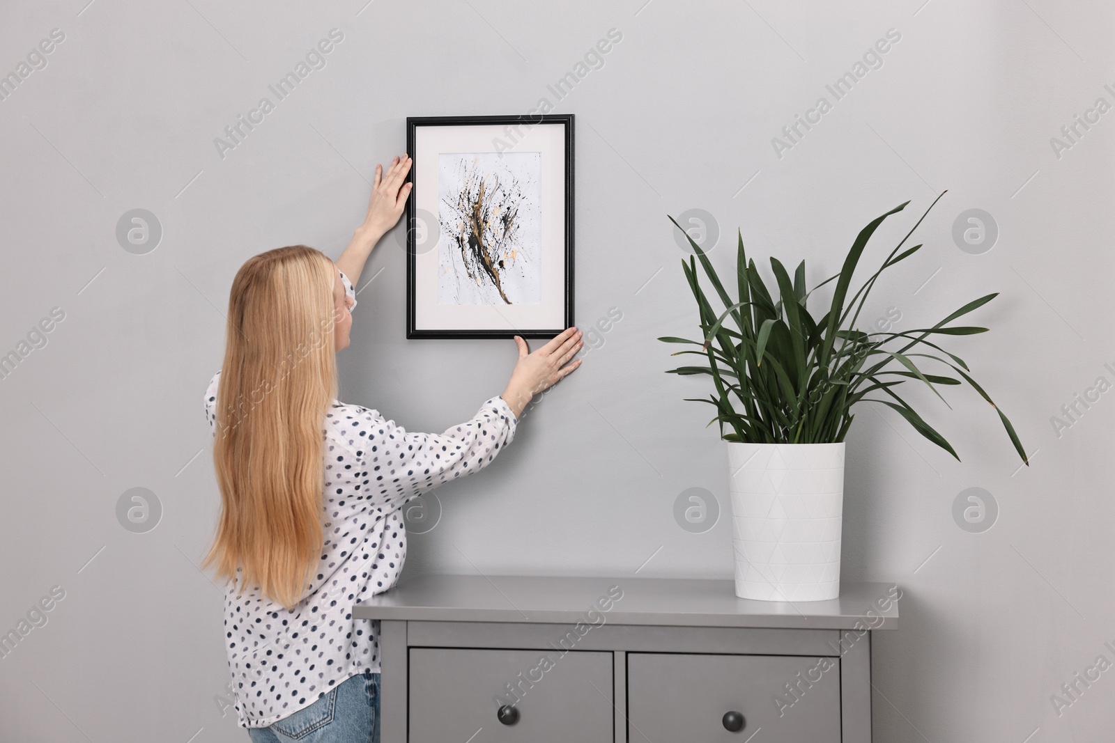 Photo of Female decorator hanging abstract picture indoors, back view