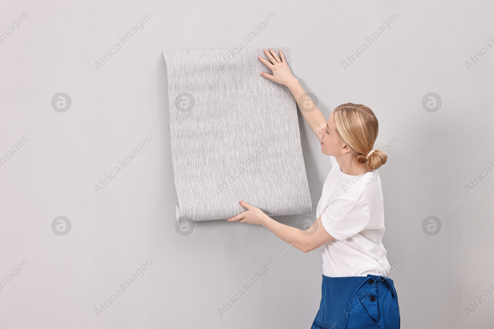 Photo of Female worker hanging grey wallpaper onto wall indoors. Space for text