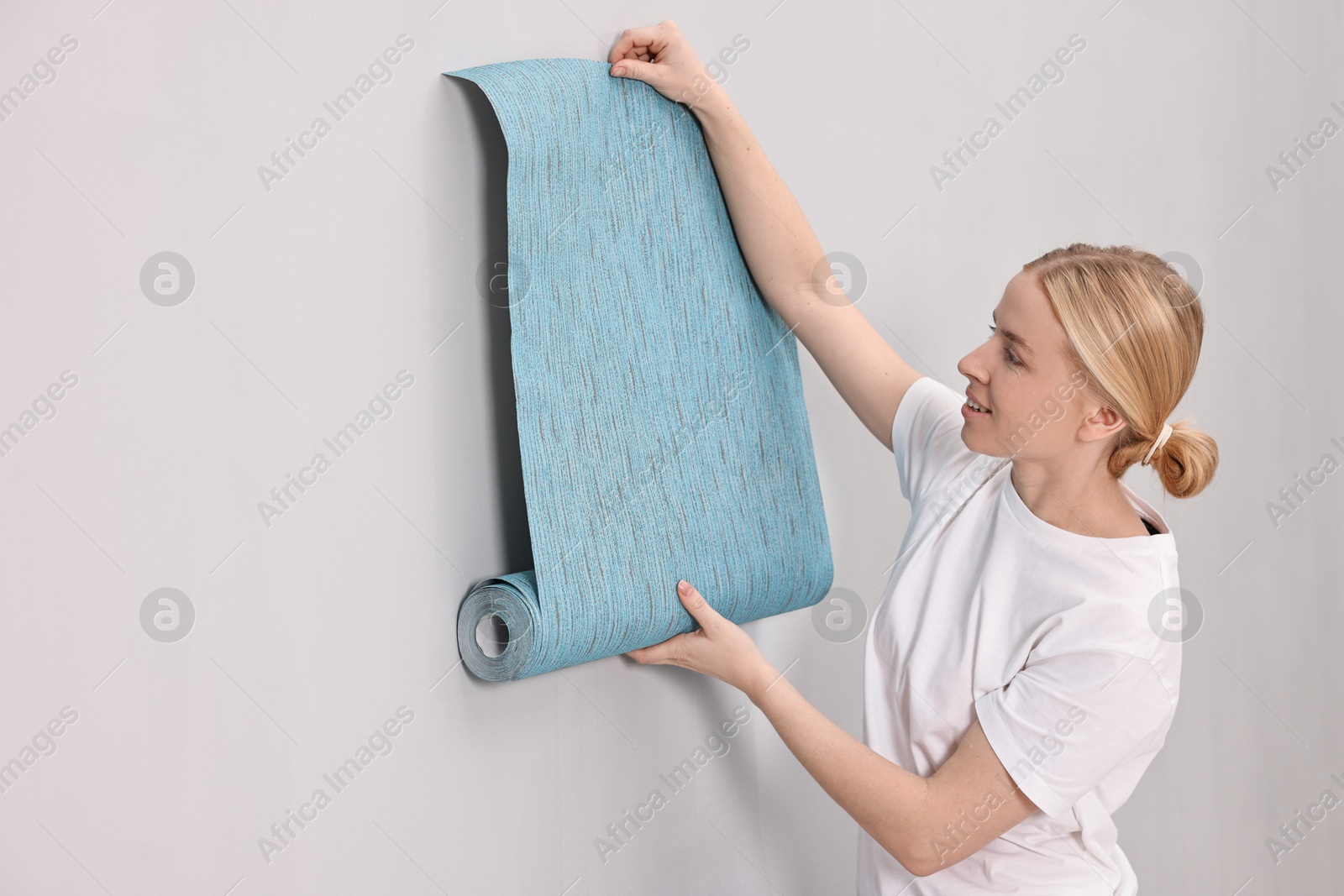 Photo of Smiling worker hanging blue wallpaper onto wall indoors. Space for text