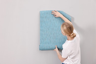 Photo of Female worker hanging blue wallpaper onto wall indoors, back view. Space for text