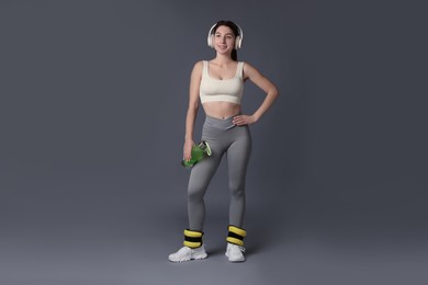 Photo of Woman in sportswear with headphones, bottle of water and ankle weights on grey background