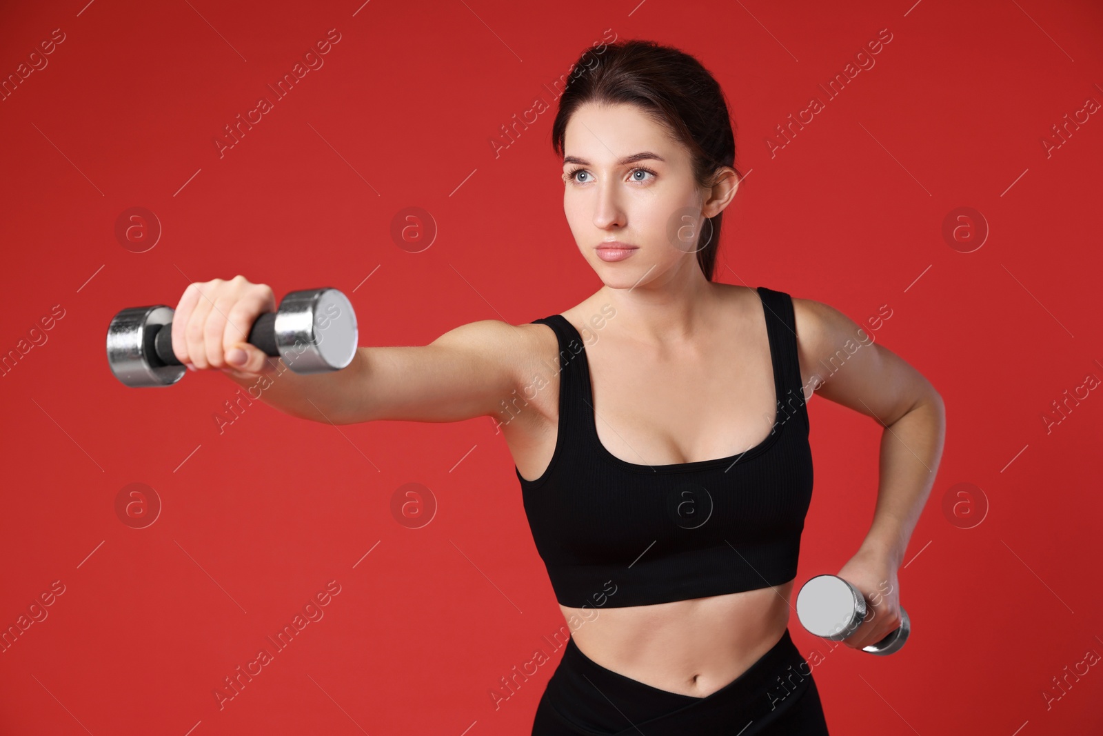 Photo of Woman in sportswear exercising with dumbbells on red background