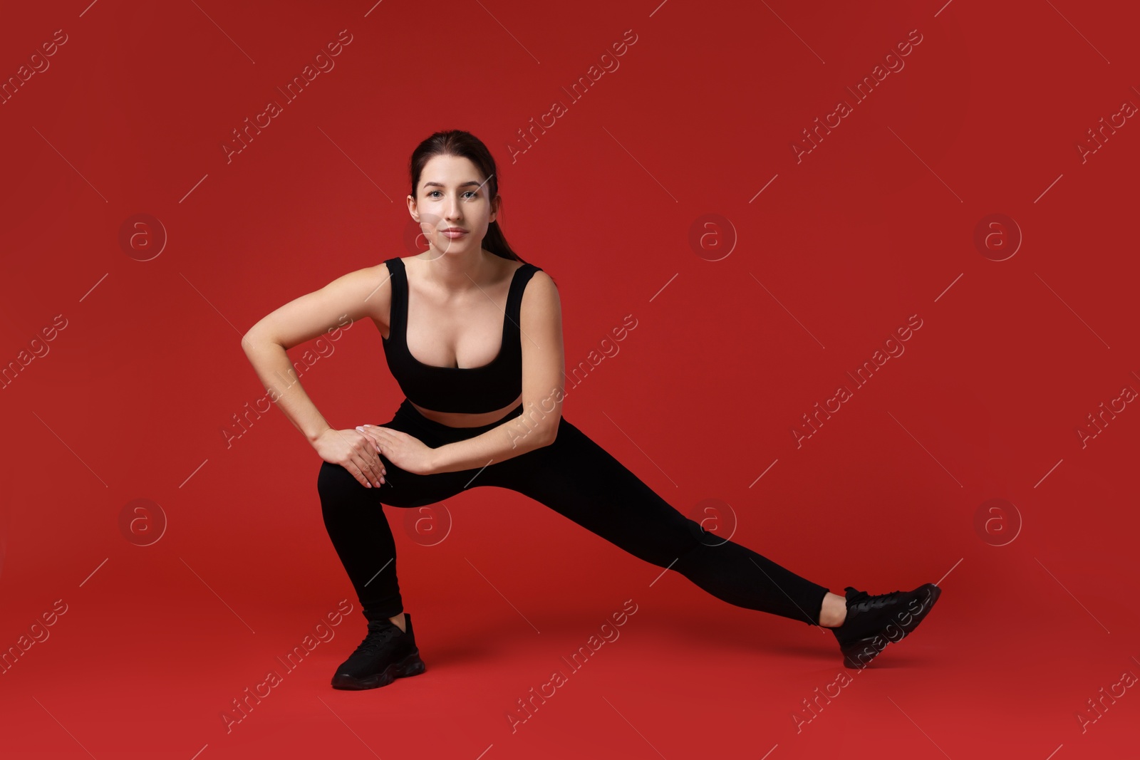 Photo of Woman in sportswear exercising on red background