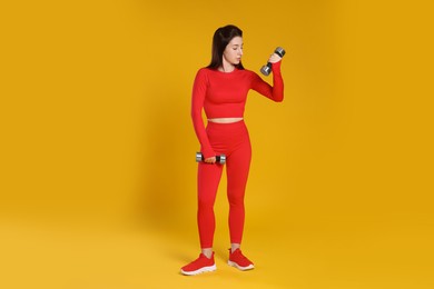 Photo of Woman in sportswear exercising with dumbbells on orange background