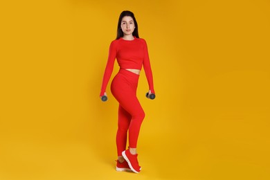 Photo of Woman in sportswear exercising with dumbbells on orange background