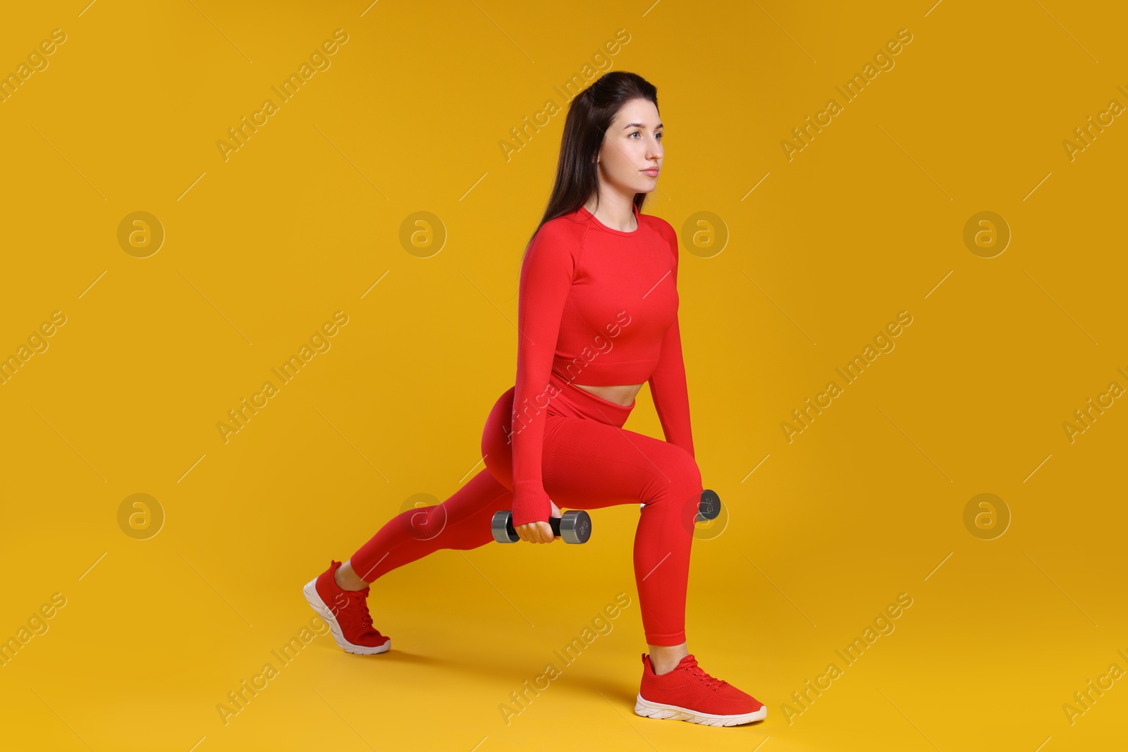 Photo of Woman in sportswear exercising with dumbbells on orange background