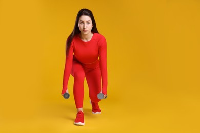 Photo of Woman in sportswear exercising with dumbbells on orange background