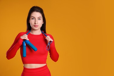 Photo of Woman in sportswear with skipping rope on orange background, space for text