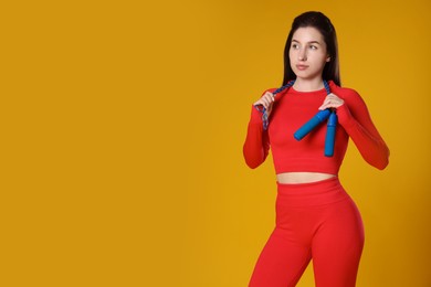 Photo of Woman in sportswear with skipping rope on orange background, space for text