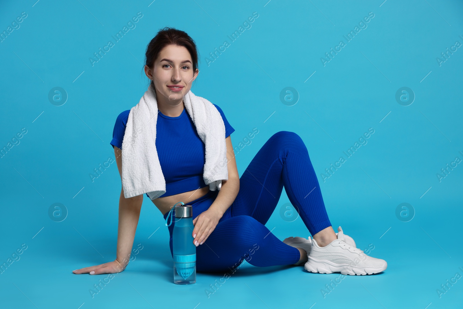 Photo of Woman in sportswear with bottle of water and towel on light blue background