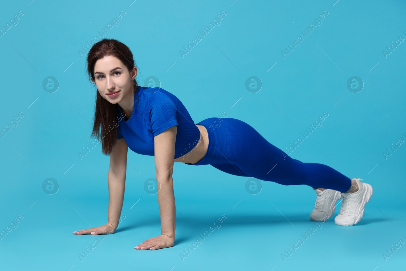 Photo of Woman in sportswear exercising on light blue background