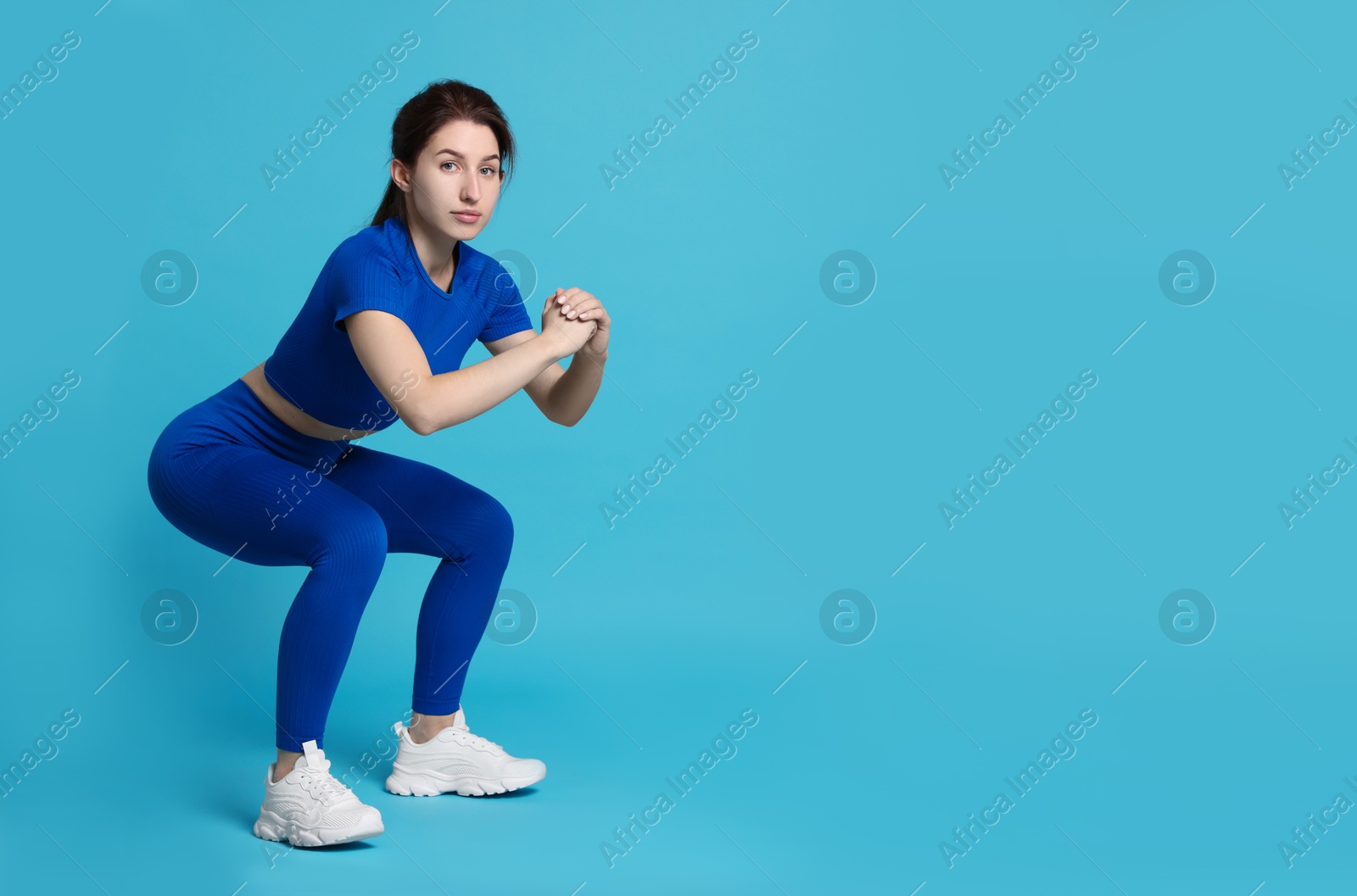 Photo of Woman in sportswear exercising on light blue background, space for text