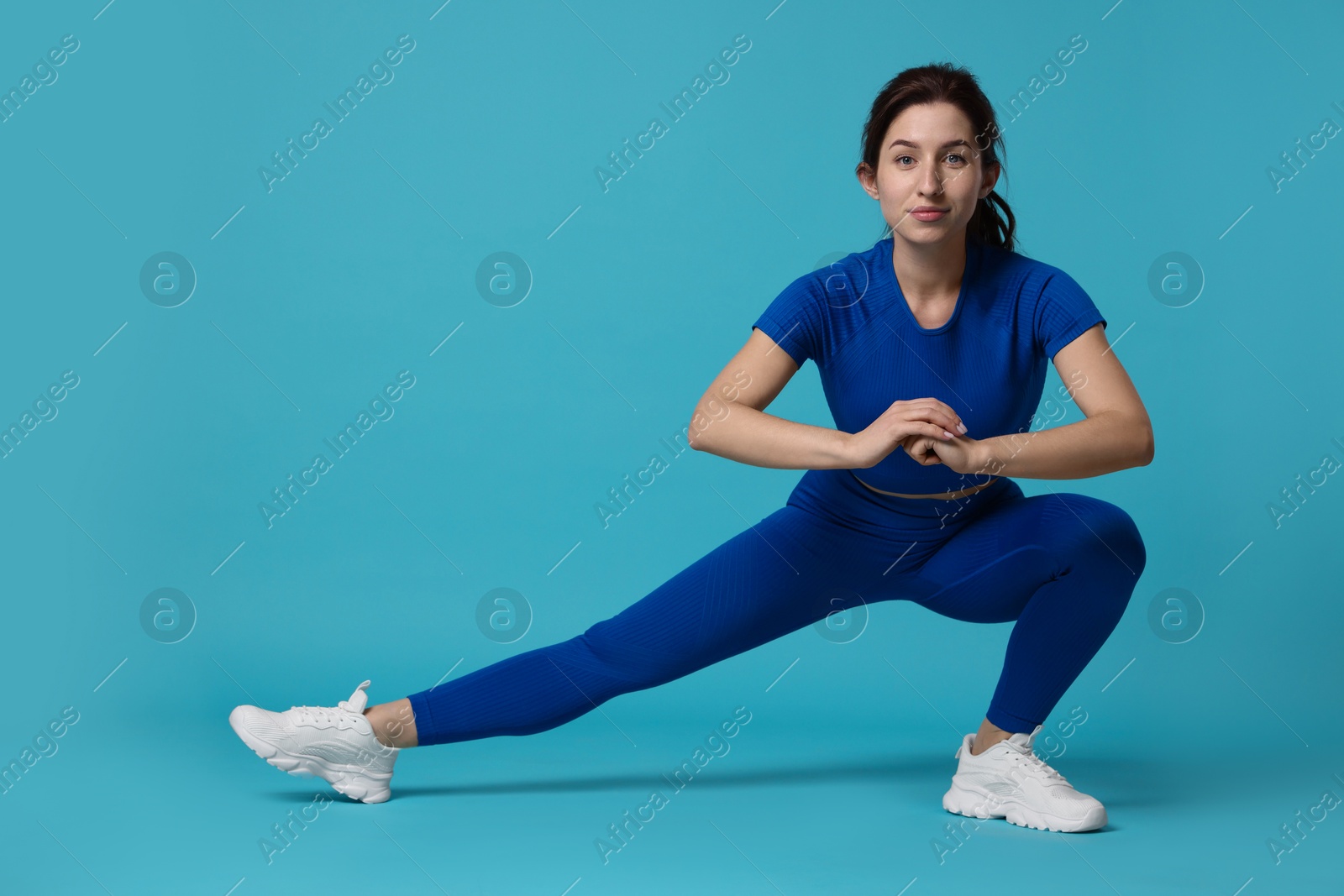 Photo of Woman in sportswear exercising on light blue background