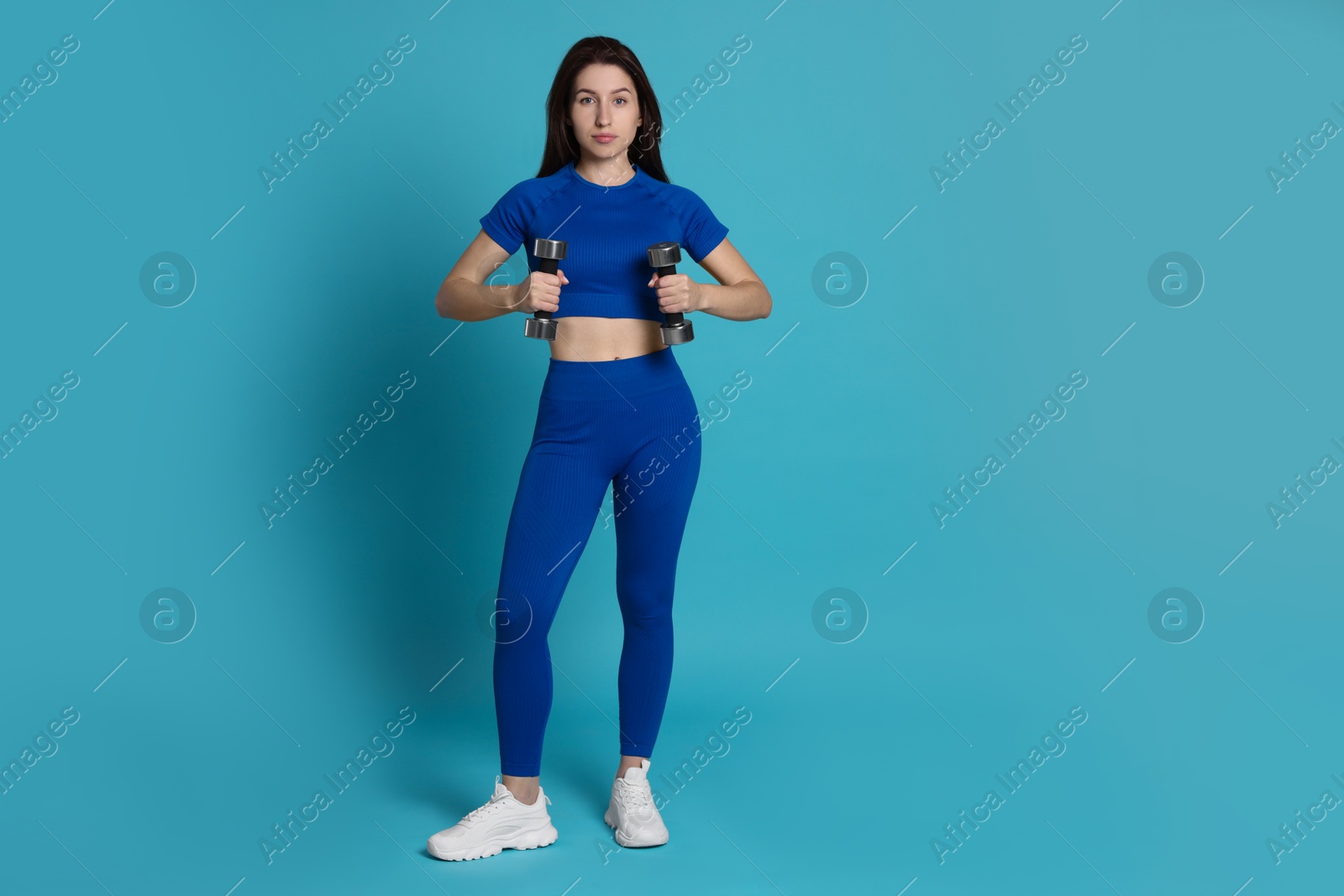 Photo of Woman in sportswear exercising with dumbbells on light blue background