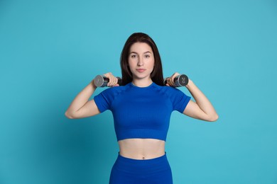 Photo of Woman in sportswear exercising with dumbbells on light blue background